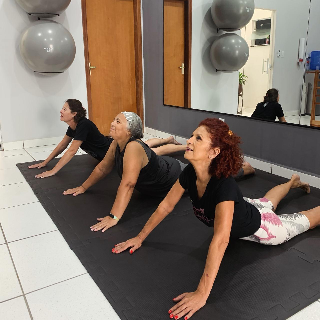 Alunas da Fabíola praticando Pilates em solo, alongando a coluna sobre o tapete